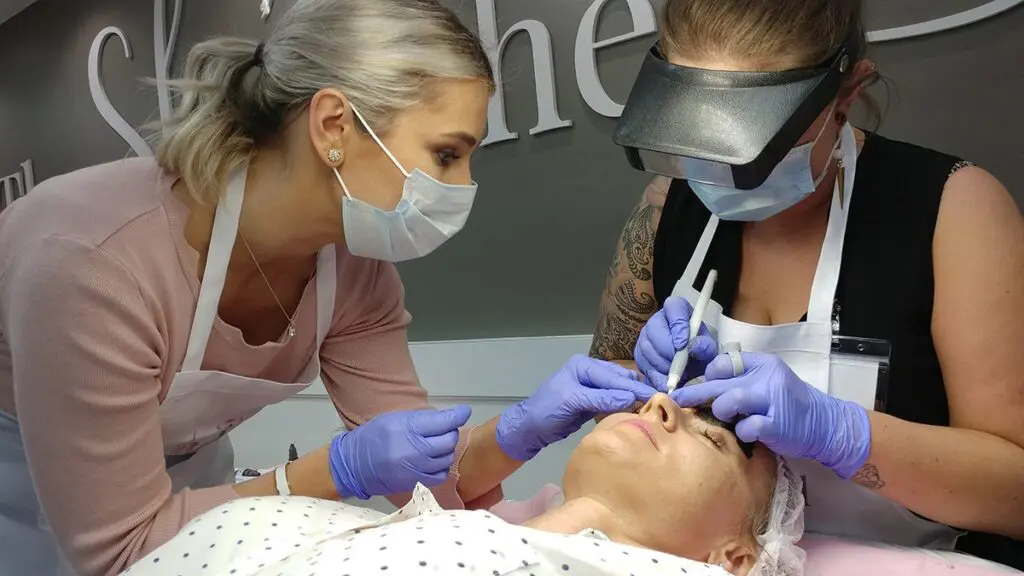 Instructor guiding a student during supervised permanent makeup work on a live model