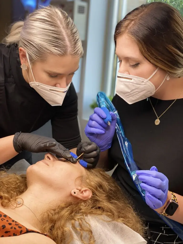 Two instructors guiding permanent makeup work on a live model